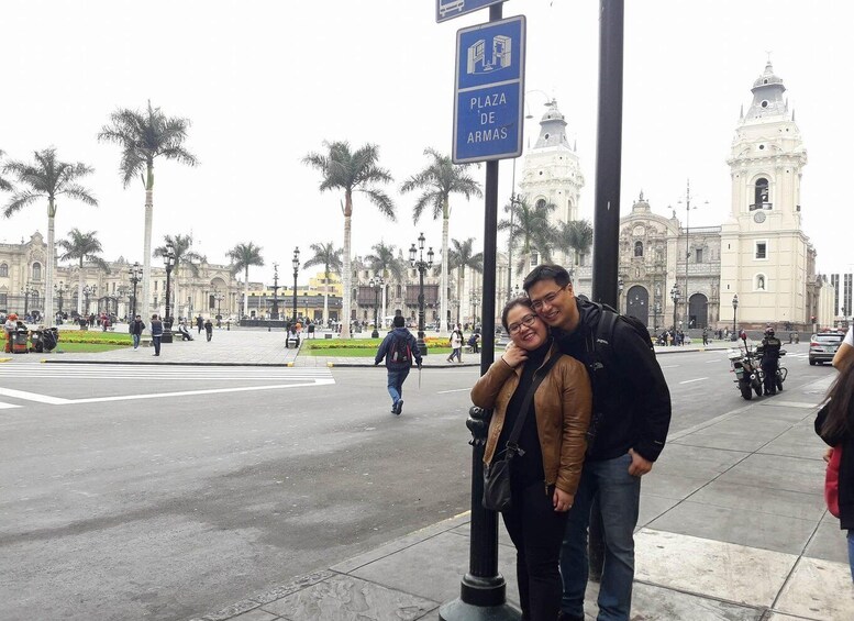 A couple posing in front of a historic plaza with palm trees and a prominent church in the background. 4