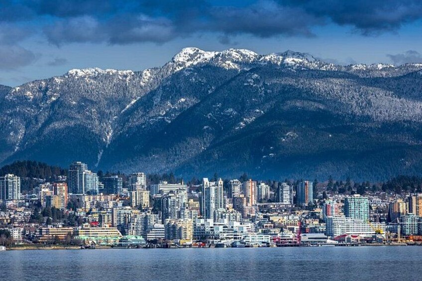A cityscape with a waterfront, high-rise buildings, and snow-capped mountains in the background. 2