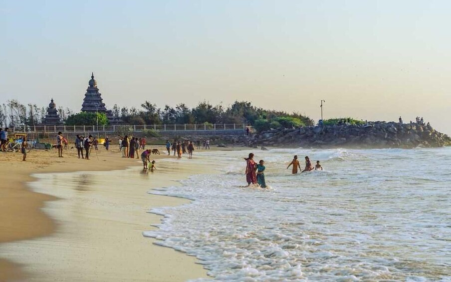 Een strand met mensen die in het water spelen en een tempel op de achtergrond. 5