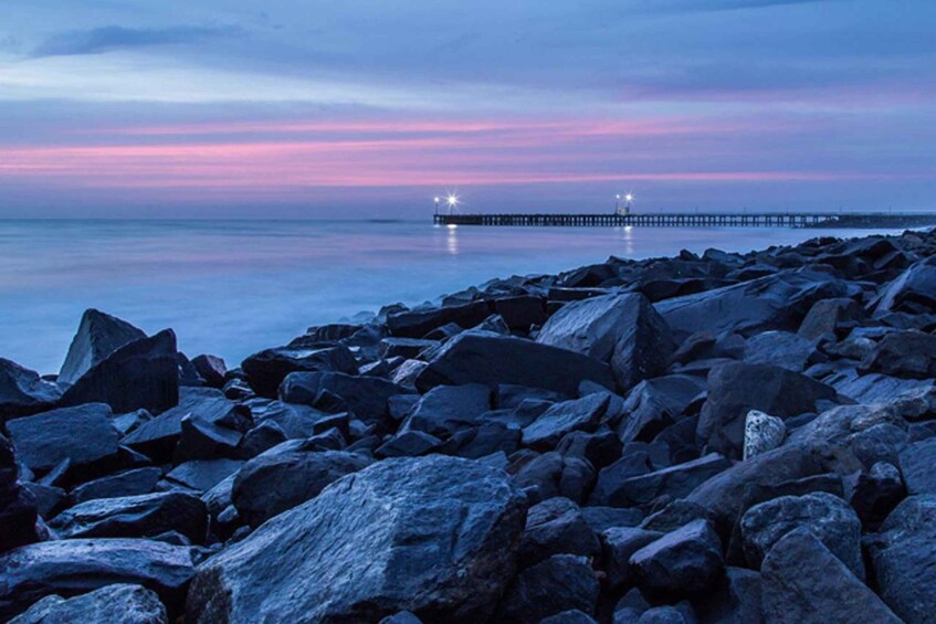 Een rotsachtige kustlijn in de schemering, met een pier die in het water uitsteekt. 2