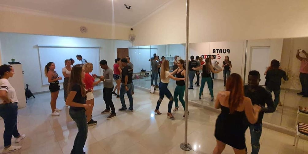 A dance class in a studio with a mirrored wall and a whiteboard. 3