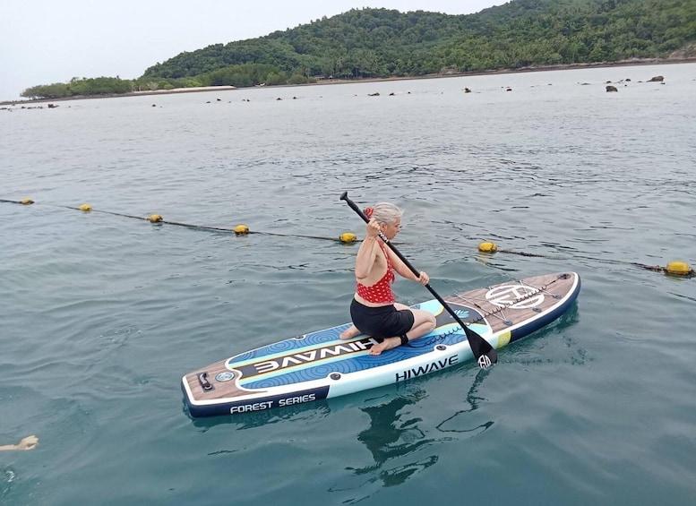 A person paddling a HIWAVE Forest Series paddleboard on calm water. 5