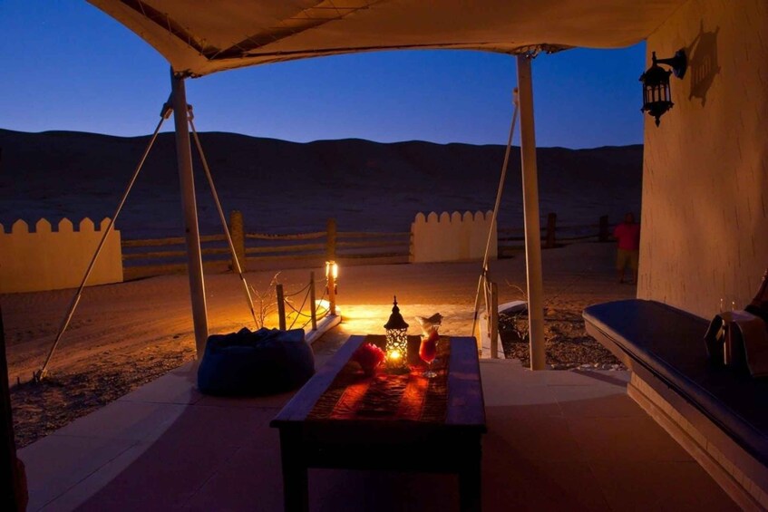 A desert camp with a table set for a meal, a lantern, and a tent. 4