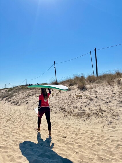 A person carrying a surfboard on a sandy beach with dunes and power lines in the background. 5