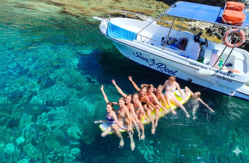 A group of people on a yellow raft in clear blue water, with a boat named 'Sunreef' nearby. 1