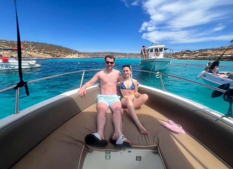 A boat with two people sitting on the deck, a clear blue sea, and a rocky coastline in the background. 5