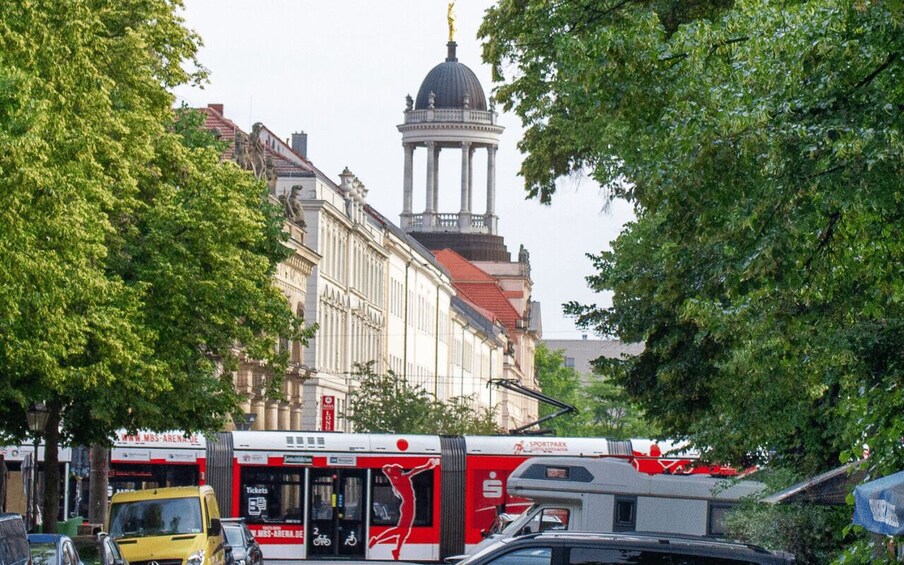 A city street with a tram, a yellow bus, and a historic building with a dome. 3