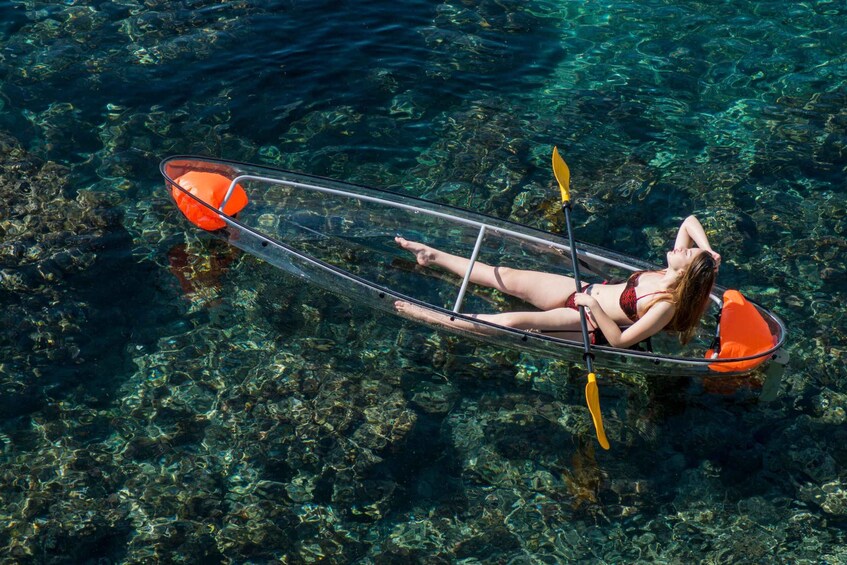 A woman in a bikini floating on a transparent kayak in clear water. 2
