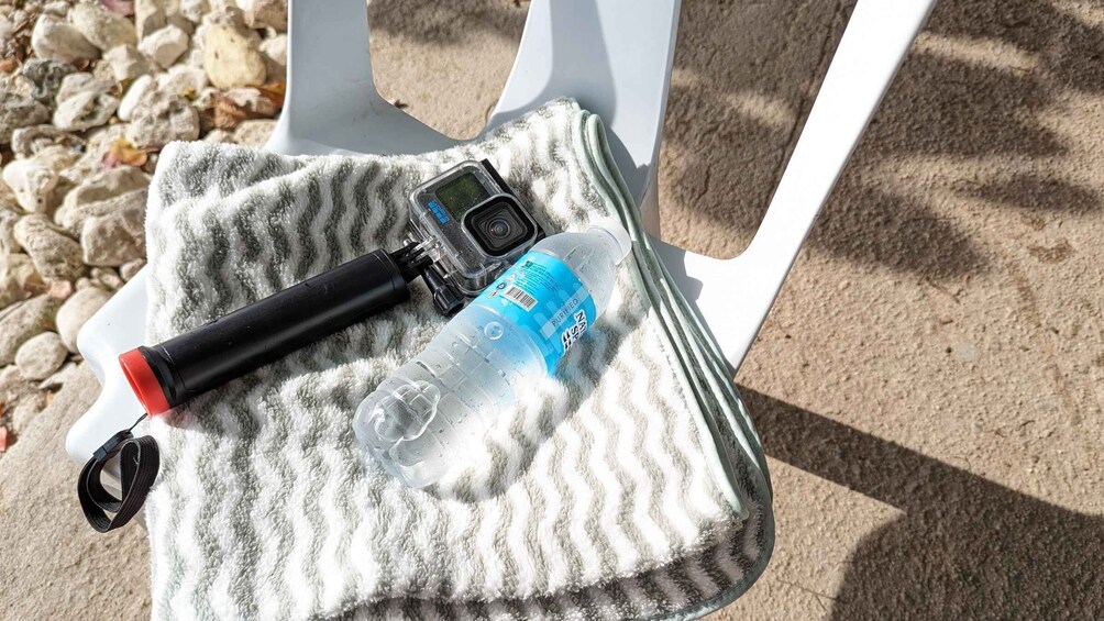 A black camera, a blue water bottle, and a black strap on a white towel. 2
