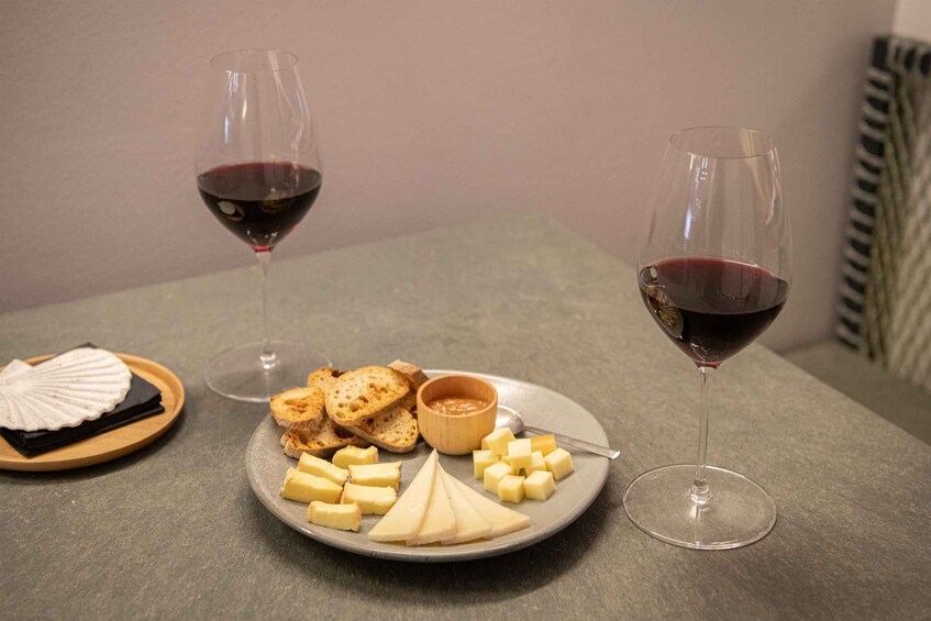 A plate with cheese, crackers, and a bowl of dip, accompanied by two glasses of red wine on a table. 1