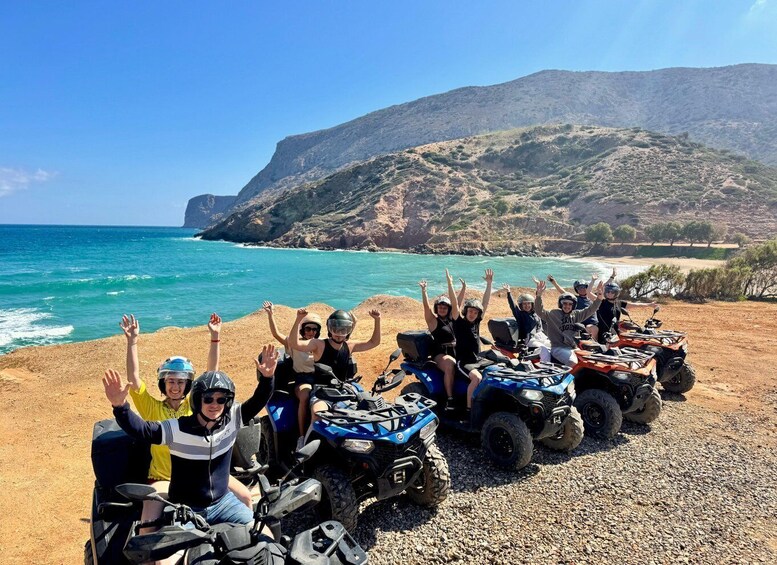A group of people on ATVs by the sea with raised hands, a rocky landscape, and a mountain in the background. 3