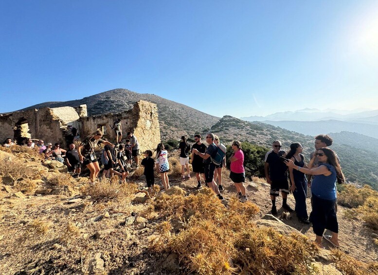 A group of people hiking on a rocky hillside with a historical ruin in the background. 3