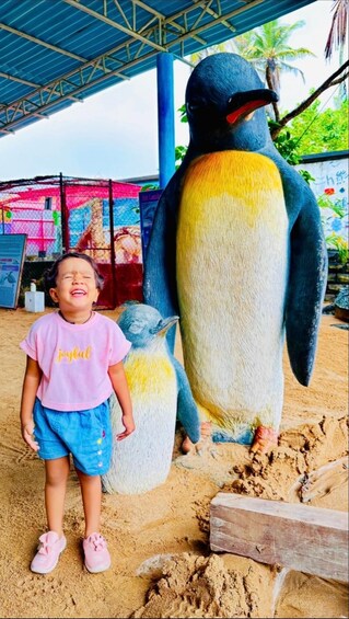 A child standing next to a large penguin statue. 5