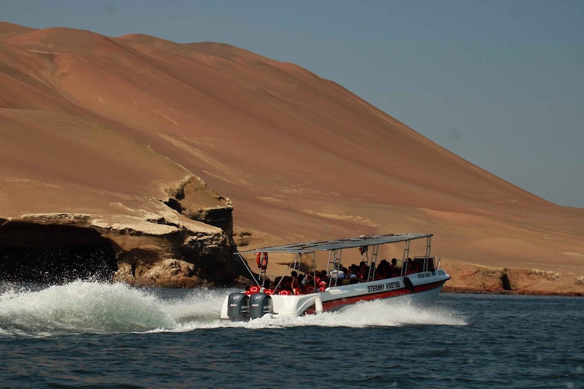 A boat with passengers navigating through a body of water near a desert landscape. 1
