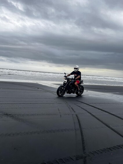 A person riding a motorcycle on a beach with waves in the background. 2
