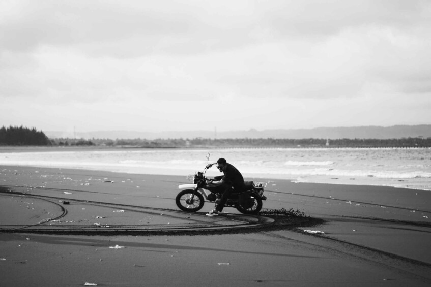 A person riding a motorcycle on a beach with waves in the background. 3