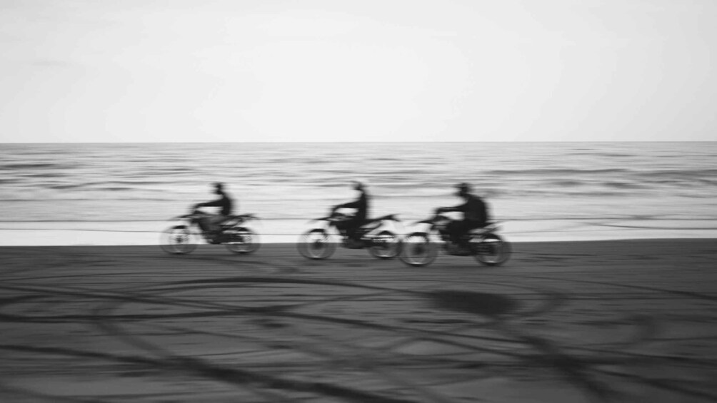 Three people on motorcycles on a beach with the ocean in the background. 5