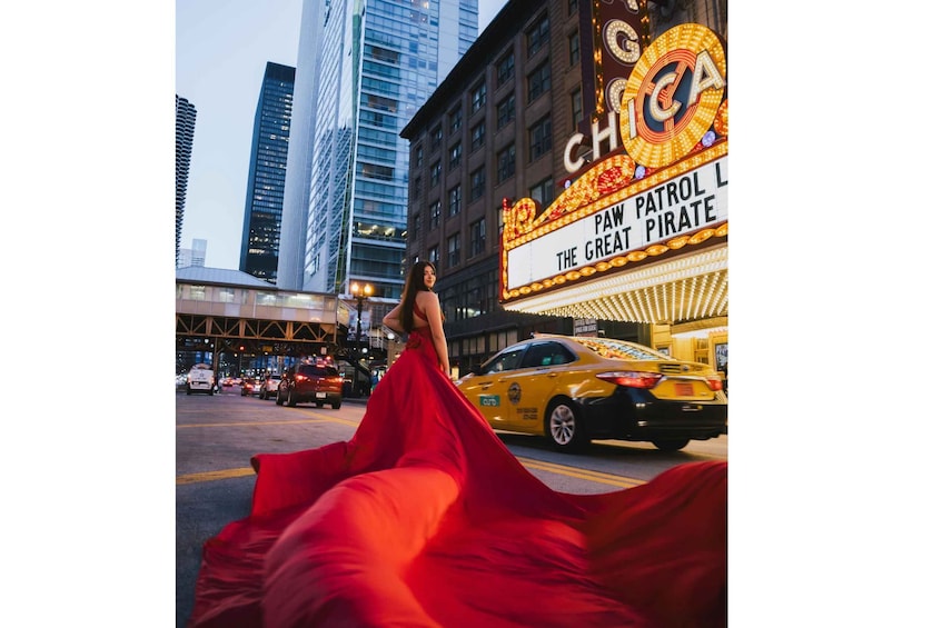 A woman in a red dress walking on a city street with tall buildings and a theater marquee. 1