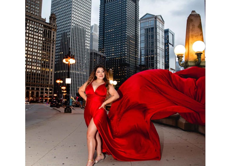 A woman in a red dress posing in a cityscape with tall buildings and street lamps. 2