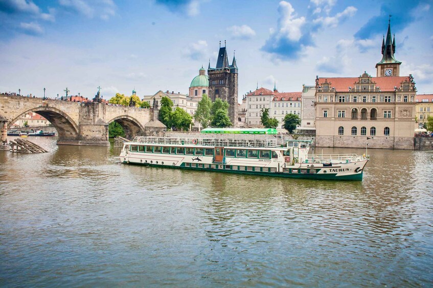 A riverboat named "Taurus" on a river with a bridge and historic buildings in the background. 1