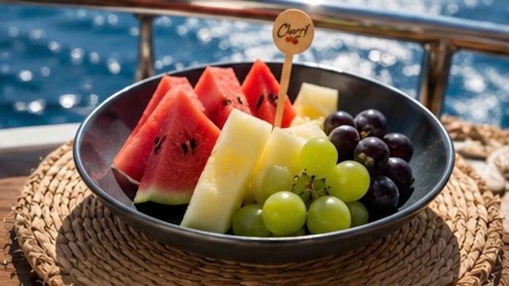 A bowl of fruit on a woven mat by a railing. 4