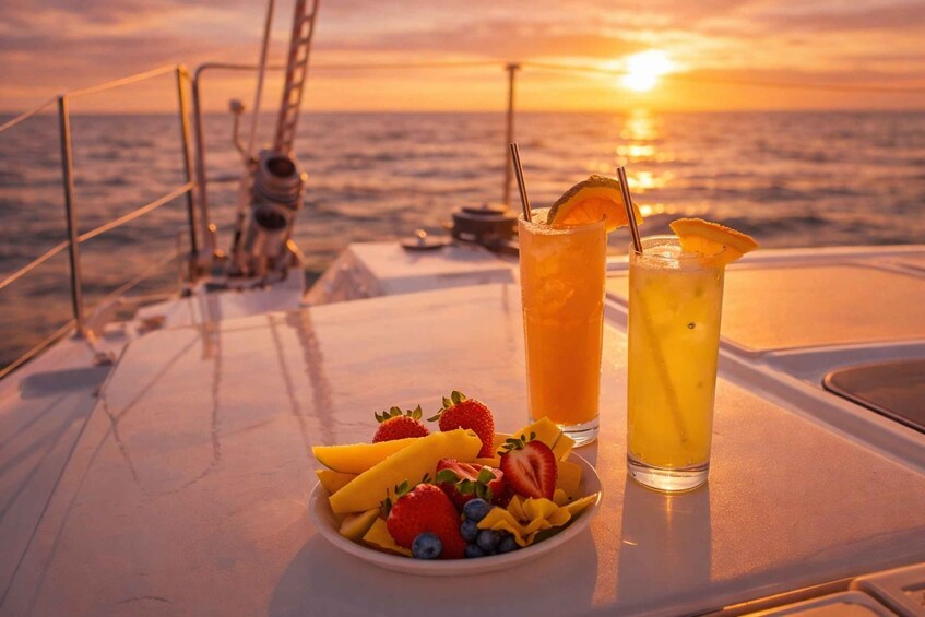 A table with fruit and two drinks on a boat with the sunset in the background. 2