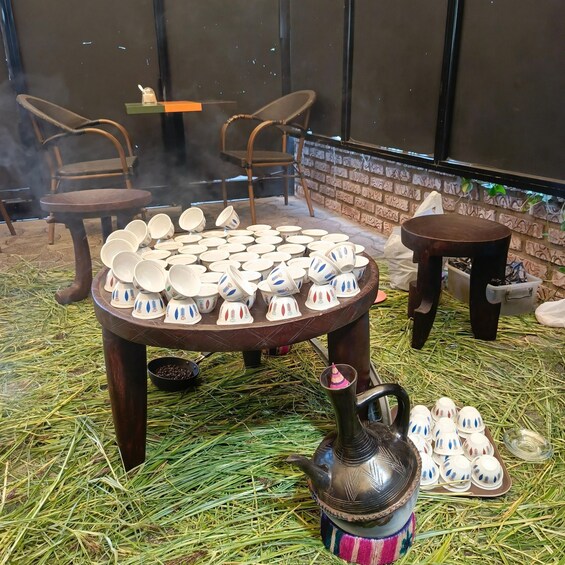 A traditional tea ceremony setup with a table of teapots and cups, a teapot, and a tray of teacups on a straw-covered floor. 5