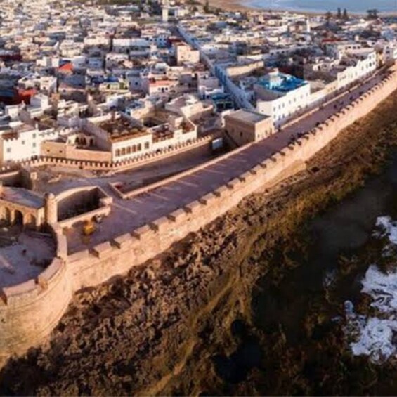 A cityscape with a prominent fortification wall, a dense cluster of buildings, and a body of water. 4