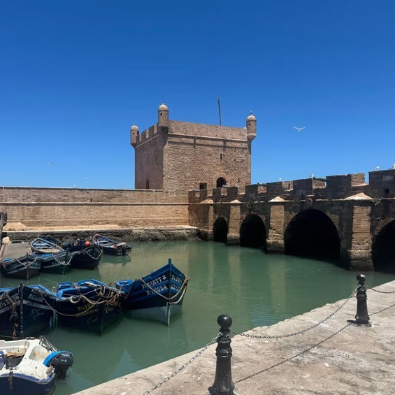 A fortified tower, a stone bridge, and moored boats in a calm harbor. 5