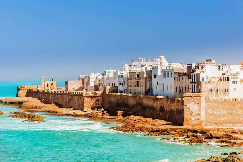 A coastal town with white buildings and a fortified wall by the sea. 1