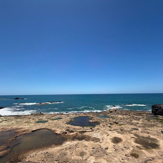 A rocky shoreline with calm sea and clear blue sky. 3