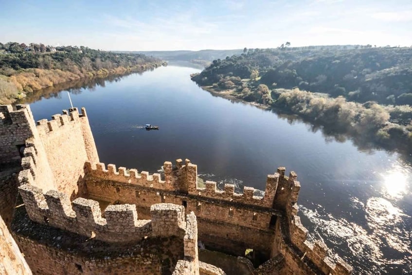A castle overlooking a calm river with a boat in the distance. 4