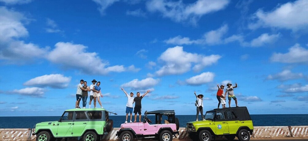 A group of people standing on four colorful off-road vehicles by the sea. 2