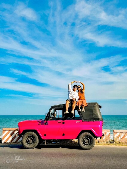 A pink jeep parked by the roadside with a clear blue sky and ocean in the background. 4