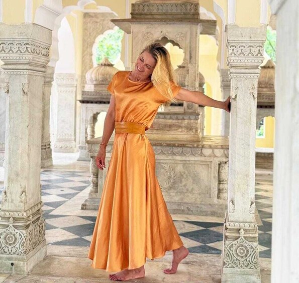 A person in an orange dress standing between ornate columns in a historical building. 5