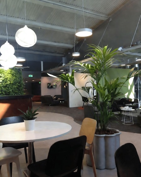 A modern office interior with round tables, black chairs, hanging pendant lights, and potted plants. 2