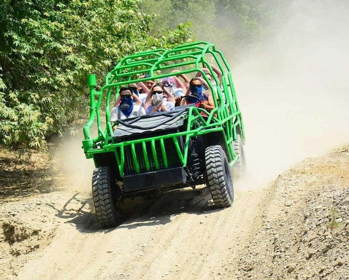 A green off-road vehicle with passengers driving on a dirt road. 2