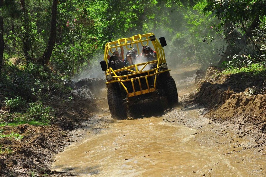 A yellow off-road vehicle driving through a muddy, forested area. 4