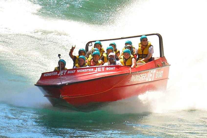 A red jet boat with 'Monster Jet Boat' written on it, carrying passengers wearing life jackets and helmets. 5