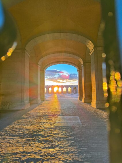 An arched stone walkway leading to a bridge with a sunset in the background. 5