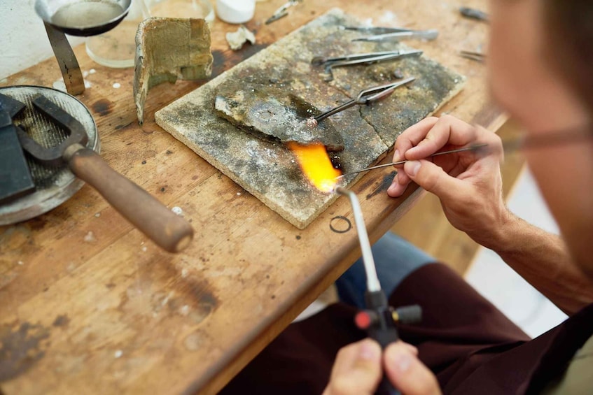 A person working with a blowtorch on a metal piece on a workbench. 3