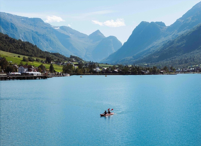 A calm lake with kayakers, surrounded by mountains and a small village. 3