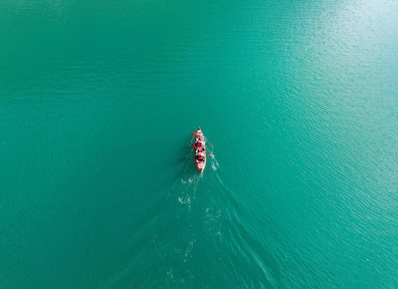 A small boat with three people rowing on turquoise water. 5