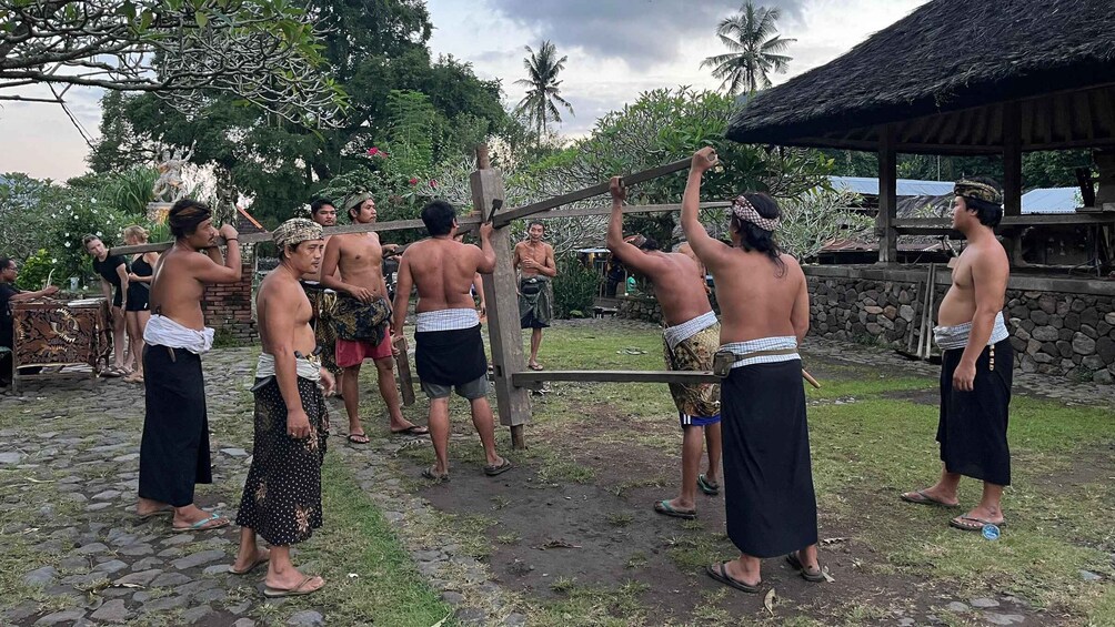 A group of people in traditional attire performing a ritual with a wooden structure in a tropical setting. 3