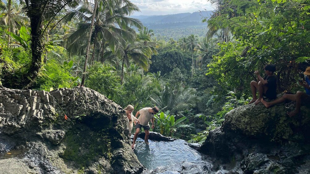 A waterfall in a tropical forest with people observing it. 1