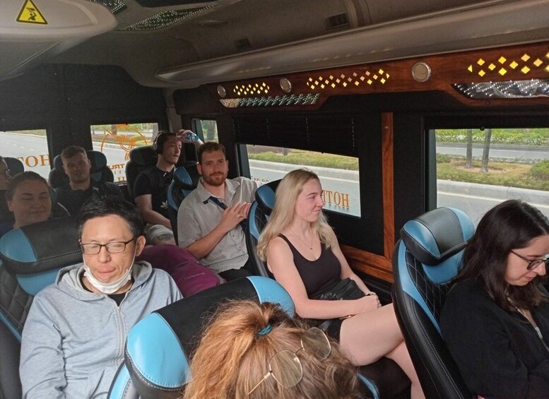 Passengers seated in a bus interior with blue seats and a wooden panel above the windows. 2