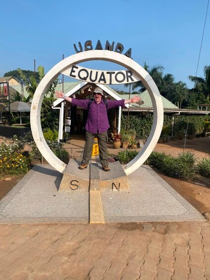 A man standing in front of a sign that reads 'UGANDA EQUATOR' with a circular design. 5