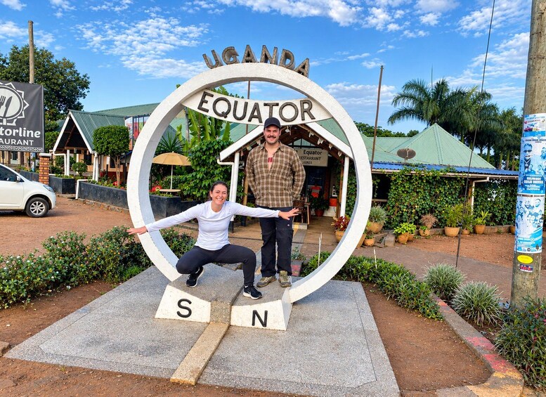 A sign for Uganda Equator Restaurant with a person posing in front of it. 2
