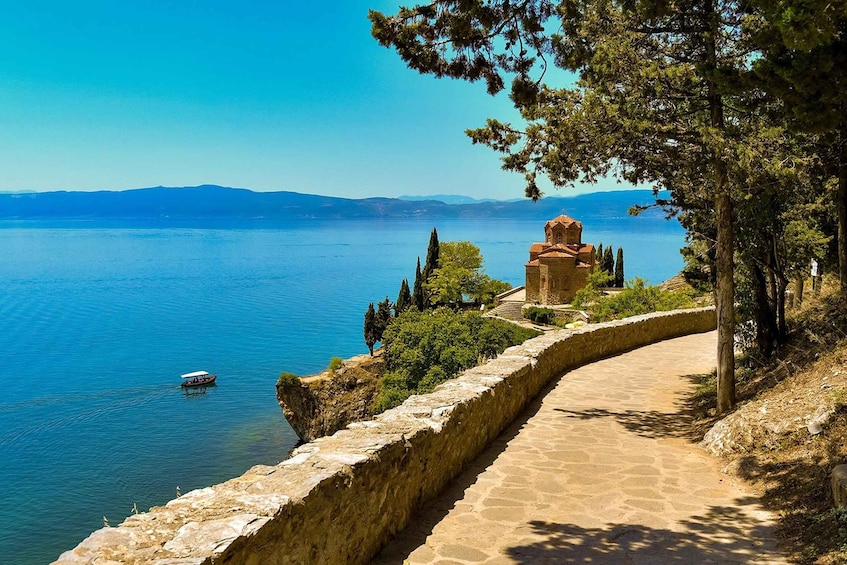 A stone pathway leading to a church by a lake with a boat in the water. 1
