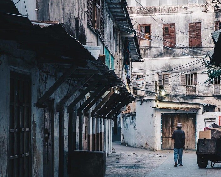 A narrow alleyway with old buildings, a man walking, and a cart. 1